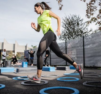 woman in green tank top and black leggings doing yoga on blue round trampoline
